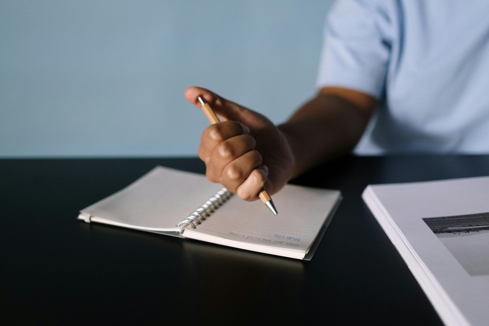 A person writing in a notebook, focusing on the hand holding a pen.